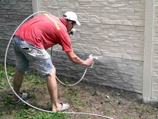 Một người đàn ông sơn một hàng rào bằng sơn trắng